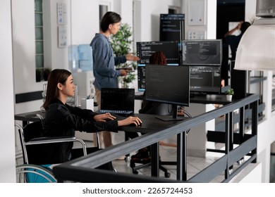 Focused software developer in wheelchair writing server code in coding agency room, using security system. Asian engineer with physical disability programming user interface ai office.