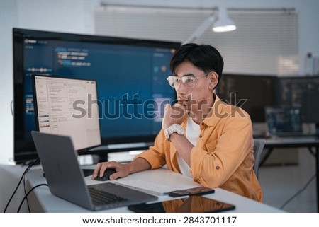 Focused software developer working on code with laptop and monitor in a contemporary office workspace for technology and innovation concepts