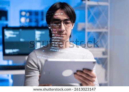 A focused software engineer is holding tablet, with coding projections on his face, symbolizing integration of technology and development in modern workspace. coding developer software engineer