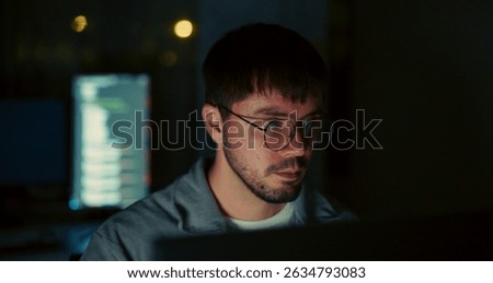 Focused software engineer works late at night in dark office. Monitor light and code reflect intense concentration and commitment in tech development.