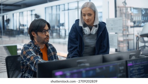 Focused Software Engineers Collaborating on Project in Modern Office. Male Developer Explaining Code to Female Colleague, Both Engaged With Multiple Screens, Teamwork Through Technology.