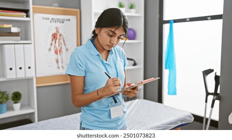 A focused south asian woman writing notes in a clinic setting, suggestive of a professional healthcare environment. - Powered by Shutterstock