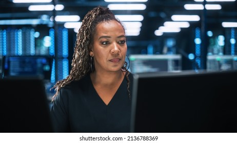 Focused IT Specialist Working on Computer in Office Environment. Diverse Multiethnic Female Developer is Using Two Monitors while Writing Code Late at the Night - Powered by Shutterstock