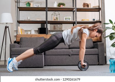 focused sportswoman exercising with ab wheel at home