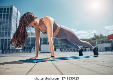 Focused Sporty Strong Young Lady Doing A High Plank Exercise On A Yoga Mat Outside