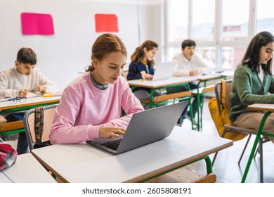 Focused students are using laptops and taking notes during a lesson in a modern classroom