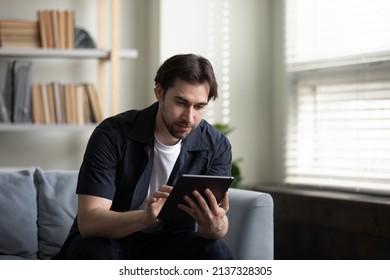 Focused tablet user man browsing internet, using online application, shopping, making video call, reading ebook, playing videogame. Millennial guy with gadget working from home, making payments