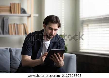 Focused tablet user man browsing internet, using online application, shopping, making video call, reading ebook, playing videogame. Millennial guy with gadget working from home, making payments
