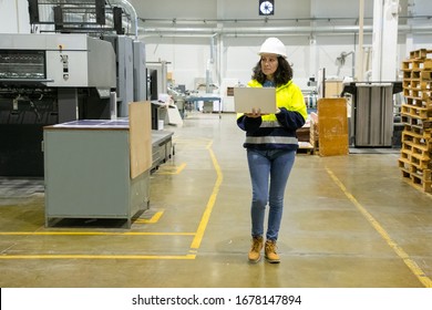 Focused Technician With Open Laptop Inspecting Factory. Concentrated Factory Employee Walking At Workplace. Print Manufacturing Concept