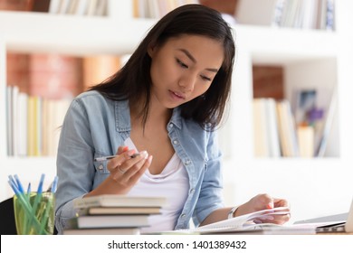 Focused Teen Asian Girl Sit At Library Desk With Stacks Of Handbook Studying Preparing For Exam, Concentrated Motivated College Female Student Write In Notebook Learning Doing Homework