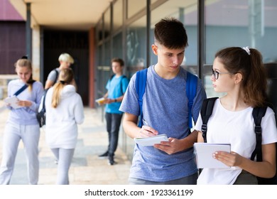 Focused teen boy talking to girl classmate outdoors in college campus, discussing schoolwork.