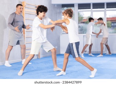 Focused teenage boys practicing close combat techniques in sparring in training room during self-defence workout under supervision of coach - Powered by Shutterstock