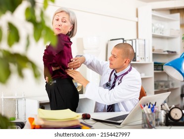 Focused therapist sitting at table in medical office, examining worried elderly female patient complaining of low back pain - Powered by Shutterstock