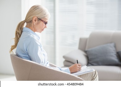 Focused Therapist Writing Notes On Sofa In Office