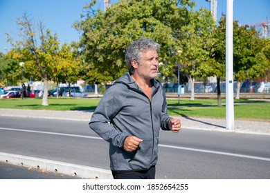 Focused Tired Mature Man Jogging Outside. Senior Jogger Training For Marathon. Medium Shot. Activity And Age Concept