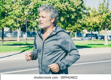 Focused Tired Mature Man Jogging Outside. Senior Jogger Training For Marathon. Medium Shot. Activity And Age Concept