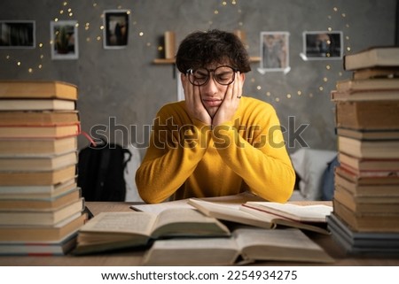 Focused tired student surrounded by books studying in a college dormitory. Copy space