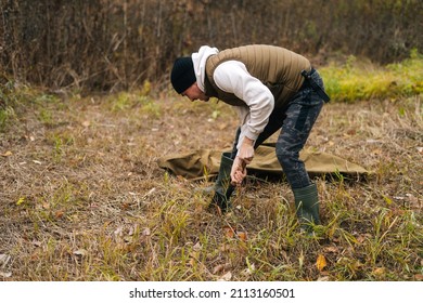 Focused tourist male wearing warm clothes digging fire place using small shovel at outdoors on cloudy overcast day. Concept of exploration, travel and adventure in nature. - Powered by Shutterstock