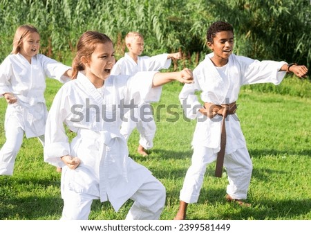 Focused tweenagers of different nationalities learning new karate moves during group class on green lawn in courtyard of sports school in summer