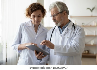 Focused two different generations doctors looking at digital tablet screen, discussing patient's illnesses or diagnosis in clinic. Young nurse assisting older male general practitioner in hospital. - Powered by Shutterstock