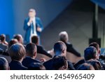 Focused view of a corporate leader speaking to an engaged audience at a professional business conference. The blurred foreground emphasizes the speaker.