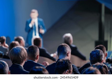 Focused view of a corporate leader speaking to an engaged audience at a professional business conference. The blurred foreground emphasizes the speaker. - Powered by Shutterstock