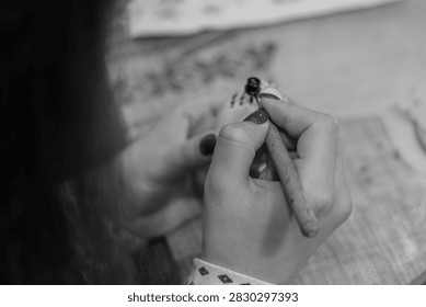 Focused view of an artisan’s hand skillfully using a traditional kistka to apply hot wax patterns onto a pysanky egg. Detailed close-up capturing the delicate craft of Ukrainian Easter egg decoration