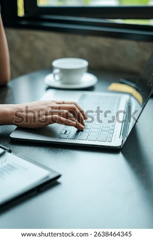 A focused view of a hand typing on a laptop in a cafÃ©, with a coffee cup nearby, capturing a modern work environment.