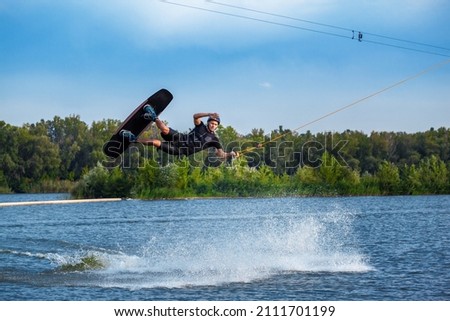 Focused wakeboarder jumping with board over calm lake water surface creating splashes