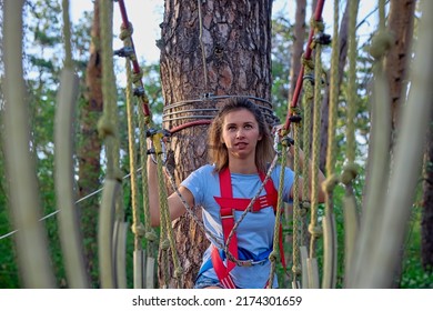 Focused woman boldly walks along a swinging suspended walkway in protective gear. Girl confidently looks up walking along the path of the rope park high above the ground