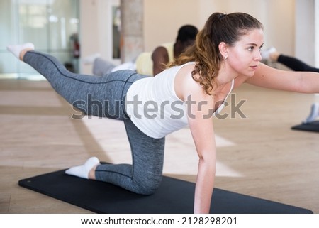 Focused woman exercising pilates with group of young adult sporty people at fitness center