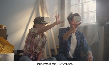 Focused Woman And Man Moving Virtual Furniture In Air Indoors. Serious Family Making Redesign With Contemporary Technologies In New Home. Young People Sitting In Headsets Among Construction Tools.