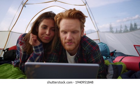 Focused Woman And Man Watching Movie On Tablet Computer In Tent. Serious Guy And Girl Looking At Screen Of Digital Tablet. Cheerful Couple Of Hikers Using Pad During Summer Weekend In Mountains