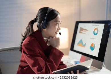 Focused woman multitasks during a video call in her home office, analyzing charts and taking notes confidently. The tech-savvy scene exudes productivity - Powered by Shutterstock