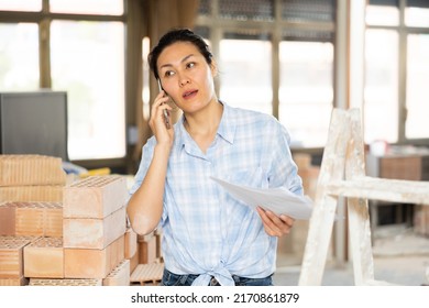 Focused woman owner of renovating house having phone talk about documents, discussing working process at construction site - Shutterstock ID 2170861879
