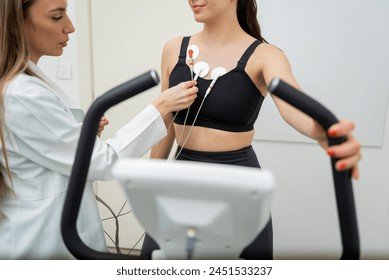 A focused woman in sportswear performs an exercise test while a professional attaches sensors to her chest. - Powered by Shutterstock