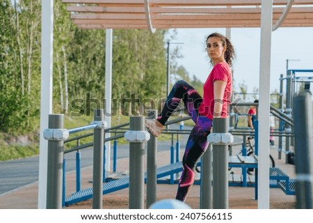 Focused woman stretching leg on outdoor gym equipment, with a lush park surrounding her