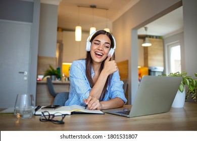Focused woman wearing headphones using laptop at home, writing notes, attractive female student learning language, watching online webinar, listening audio course, e-learning education concept