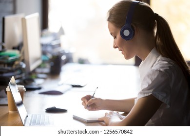 Focused woman wearing headphones write notes watch webinar study online with online teacher, young female student learning computer course with laptop listening lecture, interpreter translating class