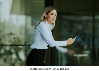 A focused woman in a white blouse engrossed in her smartphone outside a sleek modern office building on a sunny afternoon. - Powered by Shutterstock