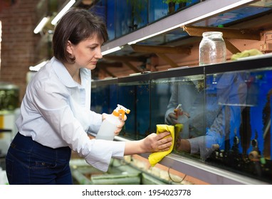 Focused Woman Working In Pet Store, Washing Glass Of Aquariums..