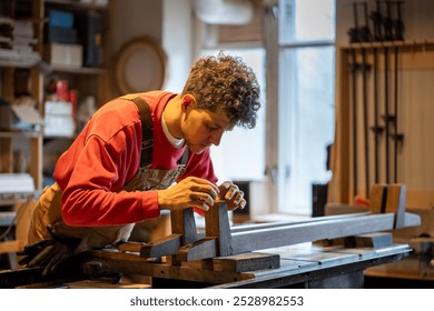 Focused woodworker applies leather pads to bed legs in workshop, enhancing stability and protection. Male craftsman using traditional woodwork methods, handmade furniture, leather work with bed frame - Powered by Shutterstock