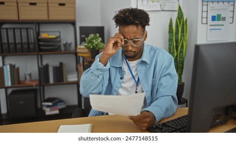 Focused young african american man in glasses working at his office desk, reviewing documents with concentration. - Powered by Shutterstock