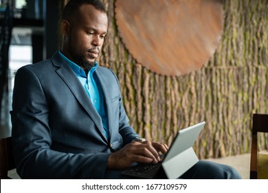 Focused Young African Businessman Sitting At A Table In The Lobby Of A Modern Office And Working On A Digital Tablet