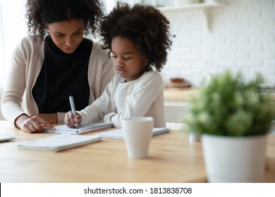 Focused young african ethnicity woman helping little biracial kid daughter with hard math or logic tasks, preparing homework at home, small mixed race girl studying with mum, homeschooling concept.