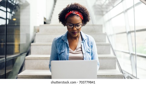 Focused Young African Female College Student Working On A Laptop On Some Stairs On Campus Preparing For An Exam