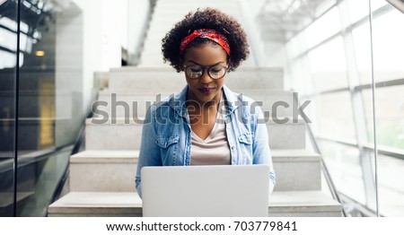 Focused young African female college student working on a laptop on some stairs on campus preparing for an exam