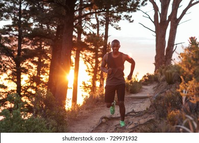 Focused young African man running alone down a trail in the forest while out for a cross country run in the late afternoon - Powered by Shutterstock