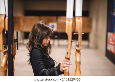 Focused young Asian woman choosing the right bow for her practice at an indoor archery range, depicting concentration and interest in the sport. - Powered by Shutterstock