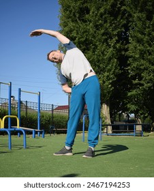 A focused young athlete dynamically performing warm-up drills and stretches outdoors. Clad in athletic gear, he meticulously prepares body for the physical demands ahead through a regimented routine